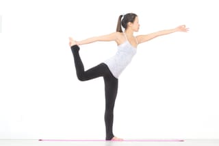 A woman in a yoga pose with one leg lifted and arms extended, on a pink mat against a white background.