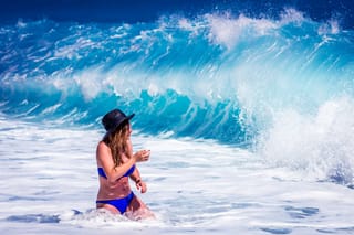 A woman in a blue bikini walking in the ocean, with waves in the background.