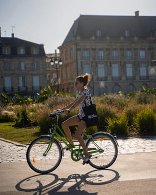 A woman riding a green bicycle on a city street with buildings in the background