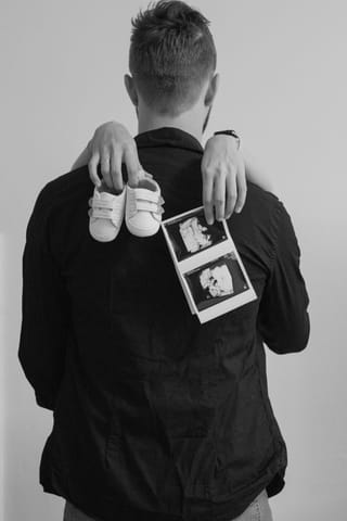 A black and white photo of a man from the back, holding baby shoes and an ultrasound scan.