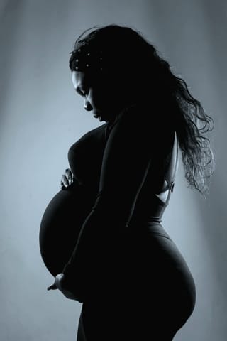 A silhouette of a pregnant woman standing in profile, holding her belly with both hands against a light background.