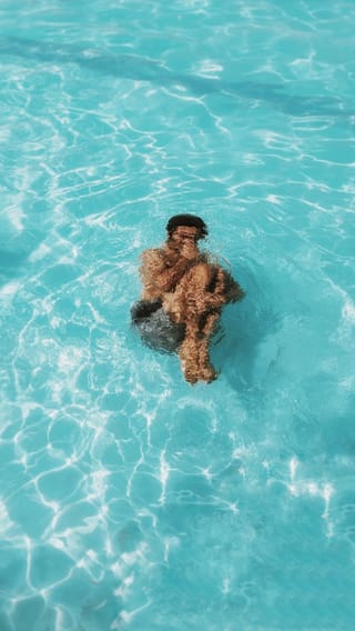 A man floating on his back in clear turquoise water with sunlight reflections.
