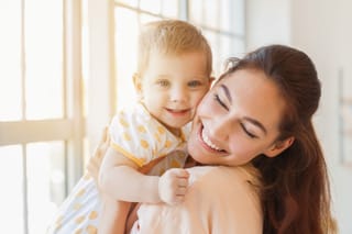 Mother hugging young child by window