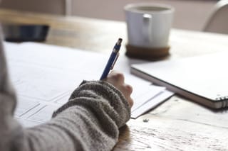 Person writing notes at desk with coffee