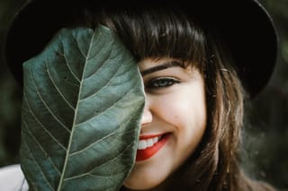 Smiling woman peeking from behind leaf