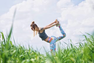 Woman practicing dancer yoga pose in a grassy field