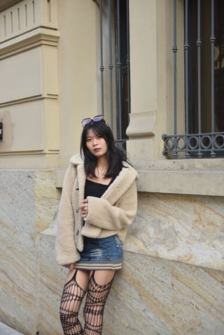 Mujer con abrigo beige y pantimedias estampadas junto a un edificio