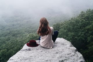 Woman sitting on a rocky cliff above a foggy forest