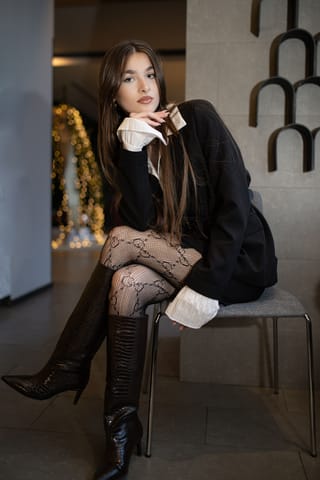 Woman seated in black outfit and fishnet tights