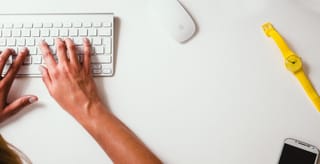 Hands typing on keyboard at white desk