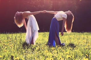 Two women performing a partner yoga stretch in a grassy field