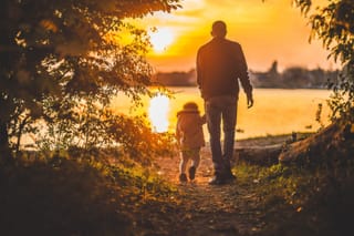 Father and young child walk together beside the water in warm sunset light