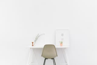 Minimalist white desk with a chair and small plants sits against a bright wall