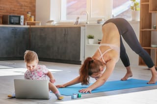 Mother practices yoga on a mat while two young children play nearby at home