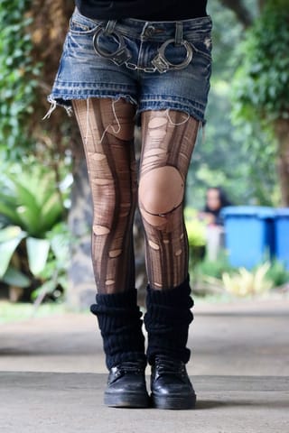 Patterned tights are paired with denim shorts, leg warmers, and dark boots outdoors