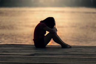 Person sits alone on a wooden dock beside calm water at sunset