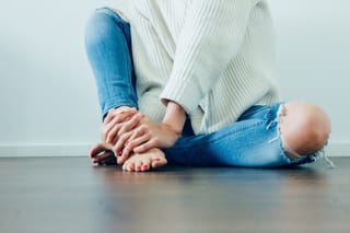 Seated person stretches forward toward their feet on a clean indoor floor