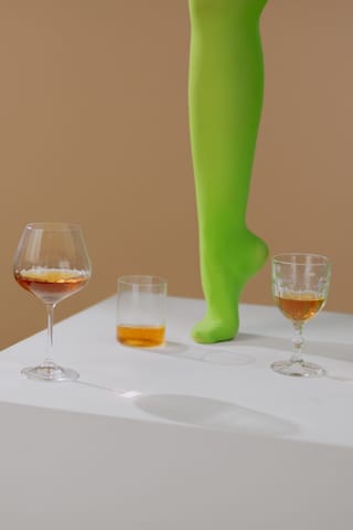 Single leg in vivid green tights stands on a tabletop beside glasses