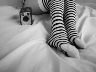 Striped knee-high socks and a vintage camera are shown on a bed in monochrome