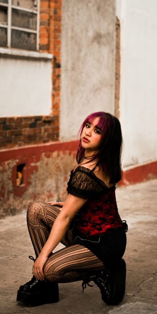 Woman crouches indoors wearing a black outfit with bold striped tights