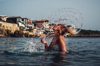 Woman flips her wet hair while standing in ocean water near the coast