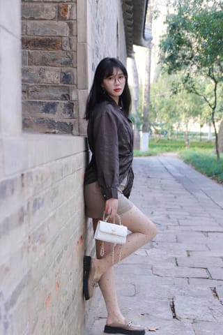 Woman holds a takeaway coffee beside a brick wall while wearing dark tights