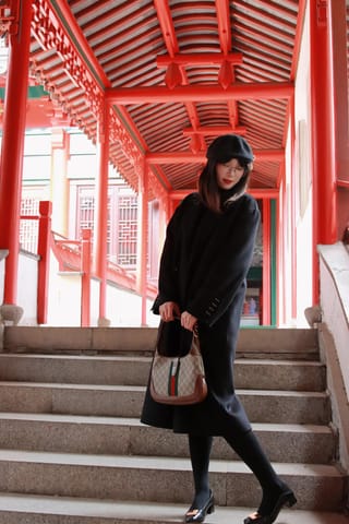 Woman in a black outfit stands on bright red stairs beneath a covered walkway