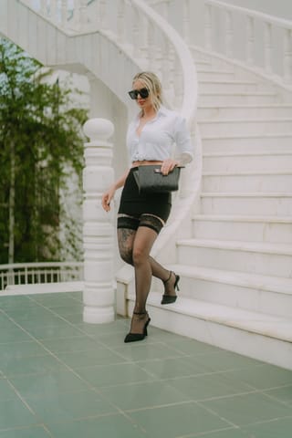 Woman poses on a porch in a black pencil skirt, sheer tights, and heels