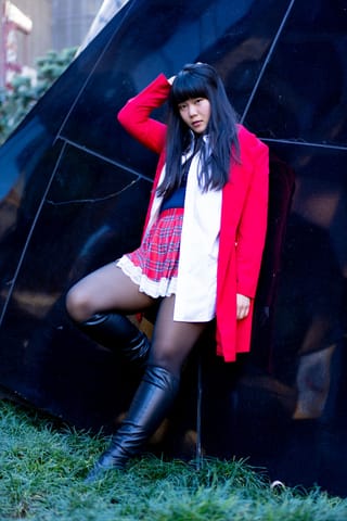Woman in a bright red coat poses outdoors wearing black thigh-high stockings and boots