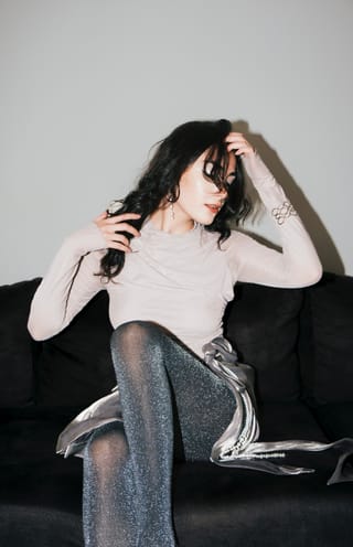 Mujer está sentada en un sofá oscuro con pantimedias grises y un top claro