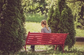 Woman sits alone on a red park bench surrounded by green trees