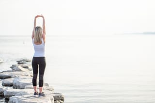 Woman stretches while standing on rocks beside a calm lake