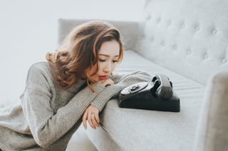 Woman lies on a bed beside a vintage black telephone in a bright room
