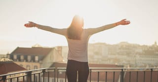 Woman stands on a rooftop with her arms outstretched toward the warm sunset