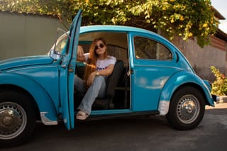 Woman sitting in the doorway of a blue Volkswagen Beetle.