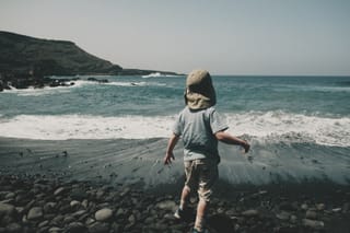 Child walking on a rocky beach beside ocean waves.