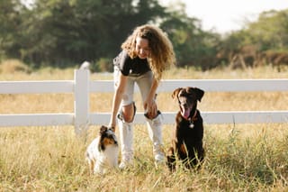 Woman with two dogs beside a white country fence.