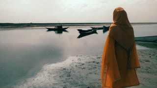 Woman in a headscarf standing by a lake with boats.