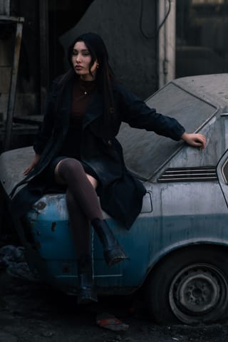 Woman in a black dress posing beside a vintage car.
