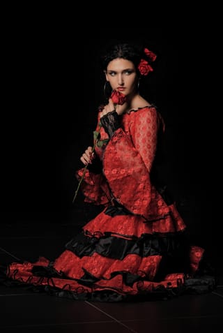 Woman posing in a red ruffled dress in a dark studio.