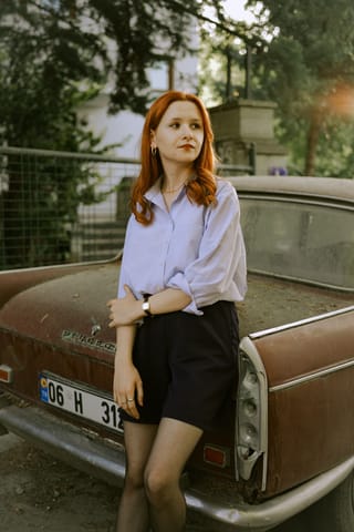 Woman posing beside a vintage car in an outdoor fashion portrait.