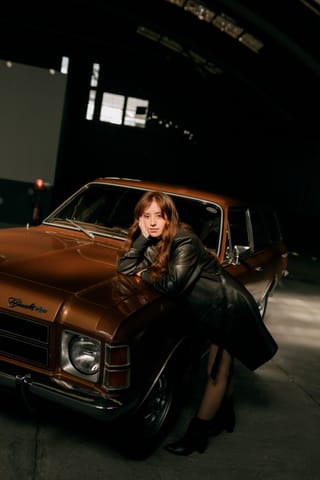 Woman posing beside a classic car inside a garage.