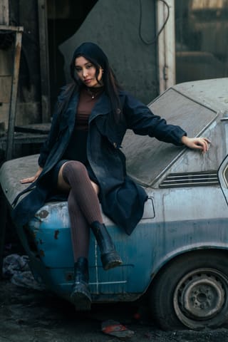 Woman in a dark coat posing against a vintage car.