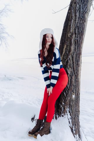 Woman in red pants and winter clothing standing in snow.