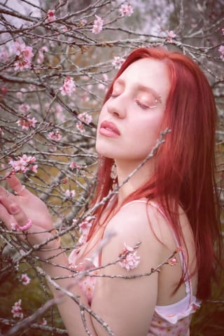 Red-haired woman posing beside pink cherry blossoms.