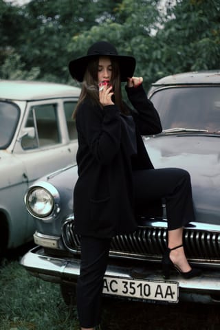 Woman in a black outfit posing beside a vintage car.
