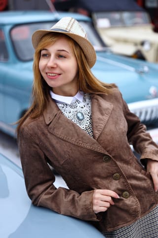 Woman wearing a brown blazer beside a vintage car.