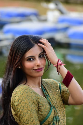 Woman in a green traditional dress and jewelry outdoors.