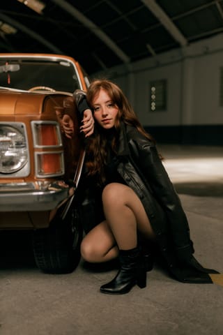 Woman in a leather coat posing beside a vintage car.