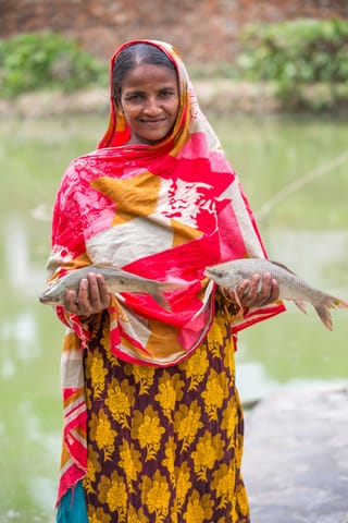 Woman holding two fish in a rural outdoor setting.